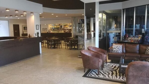 Vestíbulo de hotel con mostrador de recepción, asientos de cuero, zona de bar y vistas a través de amplias ventanas.