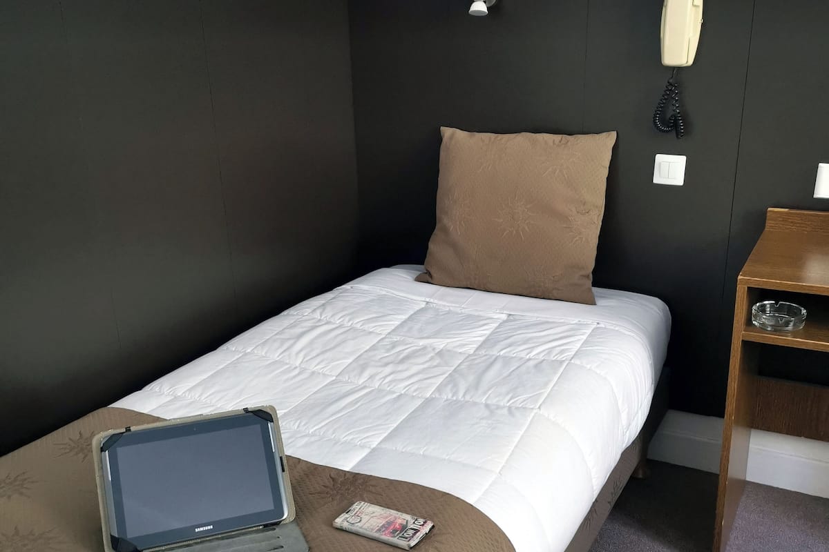 A hotel room with a single bed, a bedside table, a phone, and a tablet on the bed.