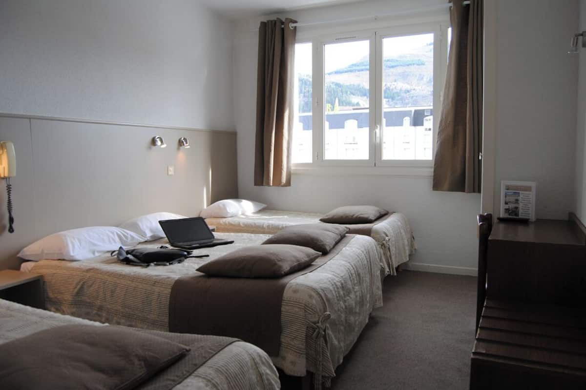 A hotel room with two beds, a desk, and a window with curtains.