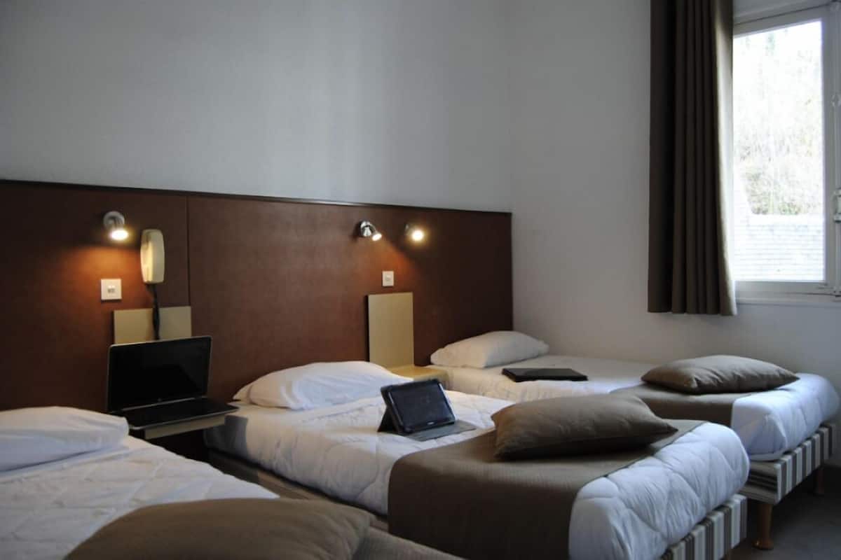 A hotel room with three beds, a desk with a laptop, and a window with curtains.