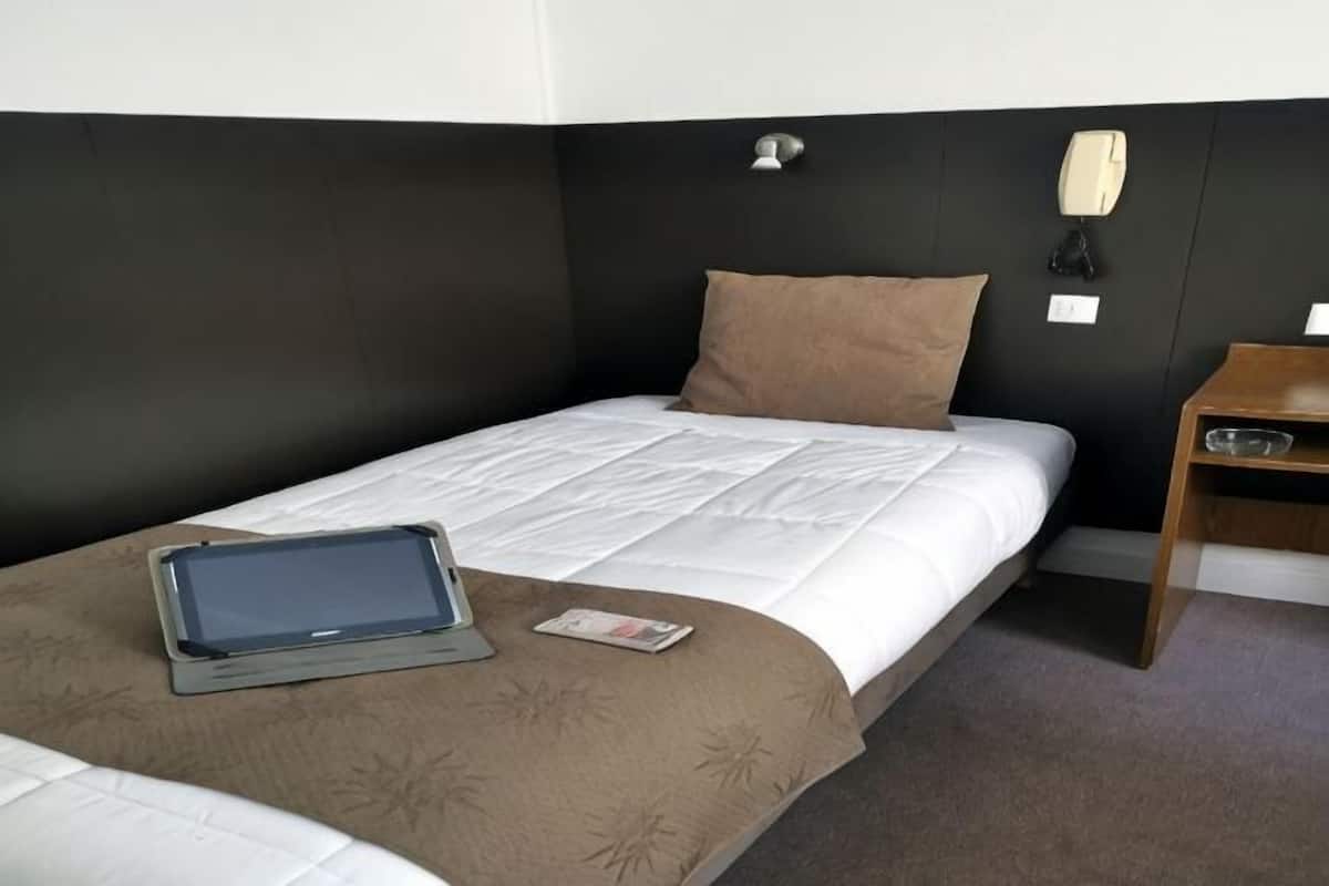 A single bed with a tablet and magazine, a bedside table, and a wall-mounted light fixture.
