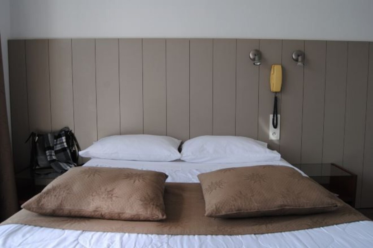 Una habitación de hotel con cama, dos almohadas, una mesita de noche y una lámpara.