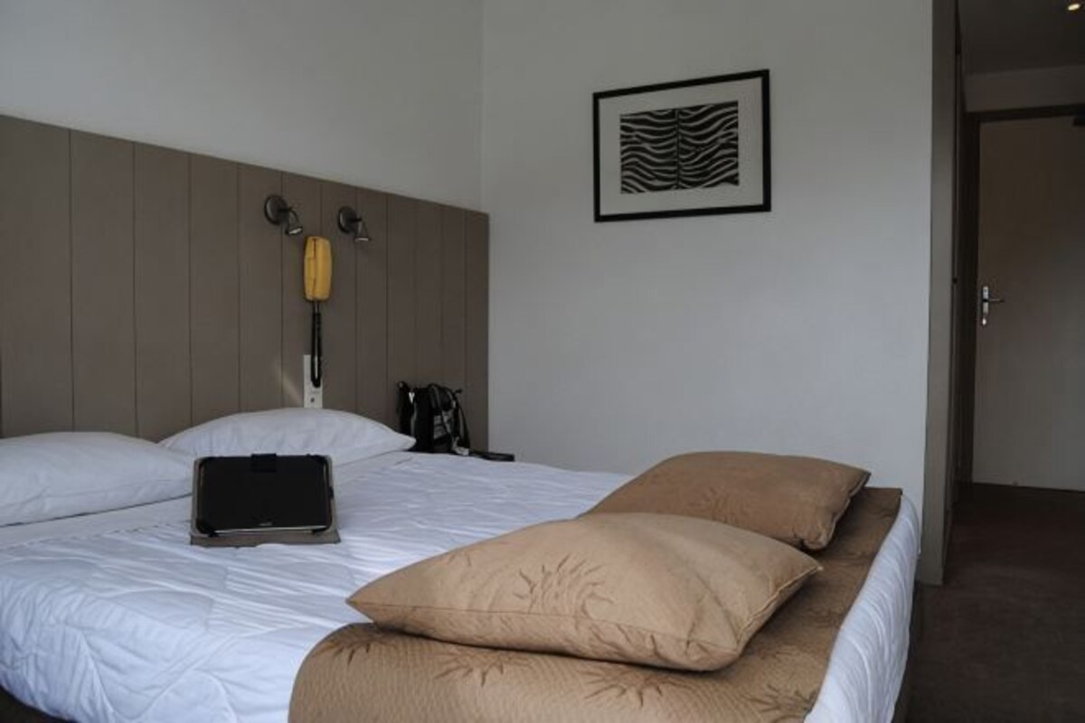 Habitación de hotel con cama, lámpara de noche, un cuadro en la pared y una puerta que da a otra habitación.