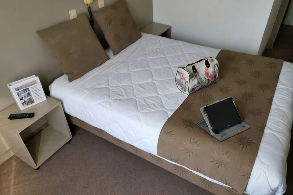 A hotel room with a bed, a nightstand, a remote control, a tablet, and a pillow with a floral pattern.