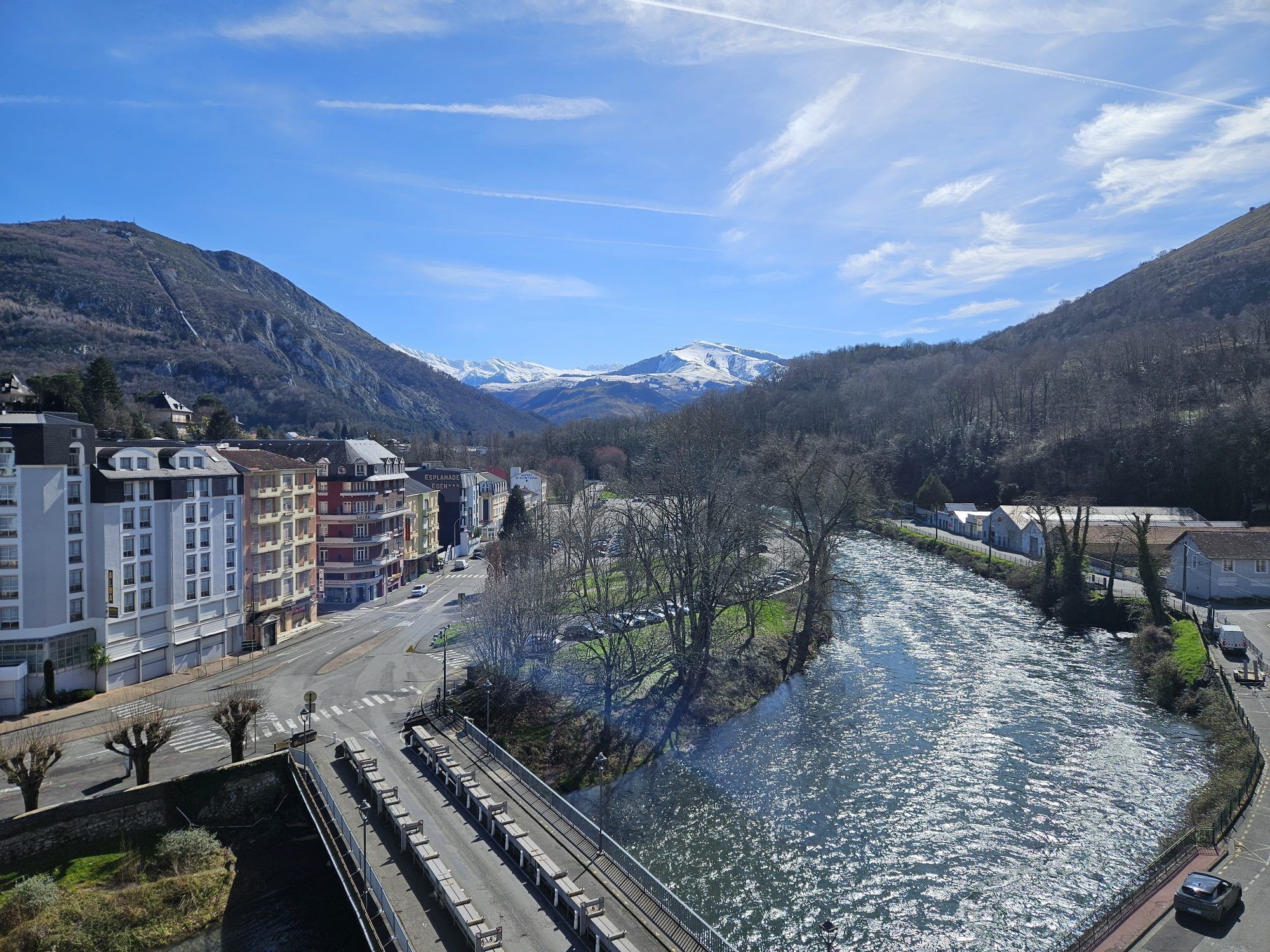 Una cittadina lungo il fiume con edifici, un ponte e montagne sullo sfondo.