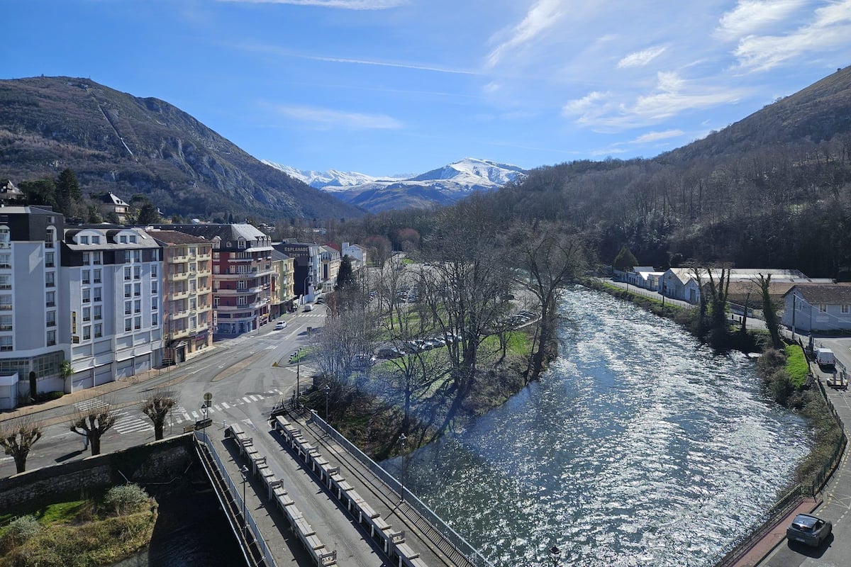 A riverside town with buildings, a bridge, and mountains in the background.