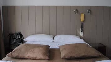 A hotel room with a bed, two pillows, a blanket, a telephone, and a wall-mounted lamp.