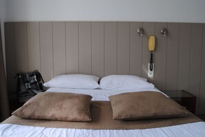 Habitación de hotel con cama, dos almohadas, manta, teléfono y lámpara de pared.