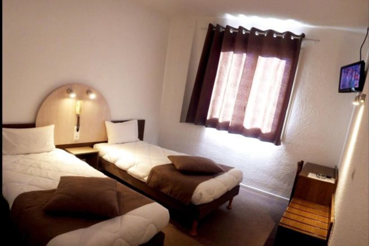 Habitación de hotel con dos camas individuales, un escritorio pequeño, un televisor y una ventana con cortinas.