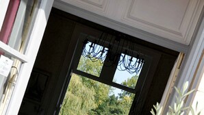 Una habitación con piso a cuadros, una silla, una mesita y un ventanal con vistas a árboles.