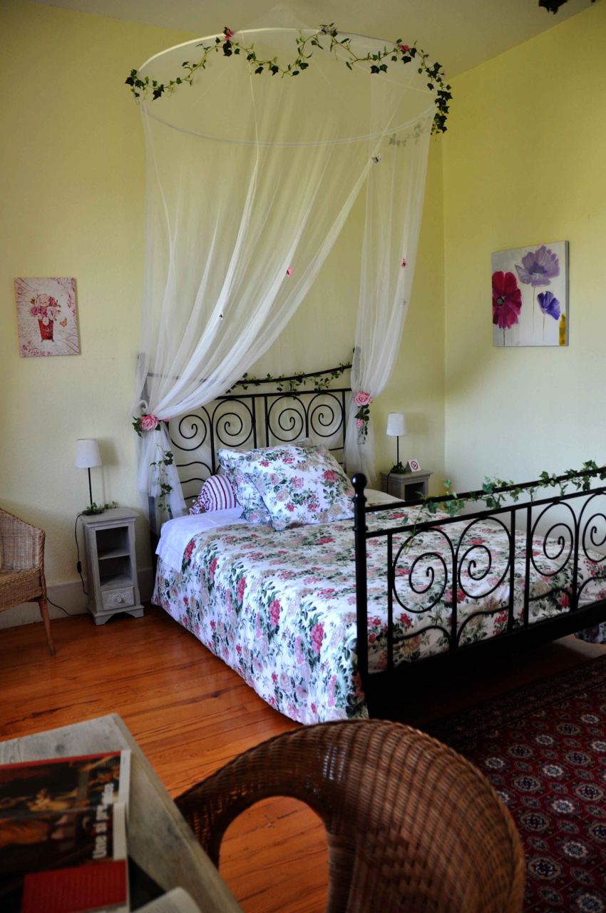 A bedroom with a four-poster bed, a bedside table with a lamp, and a chair.