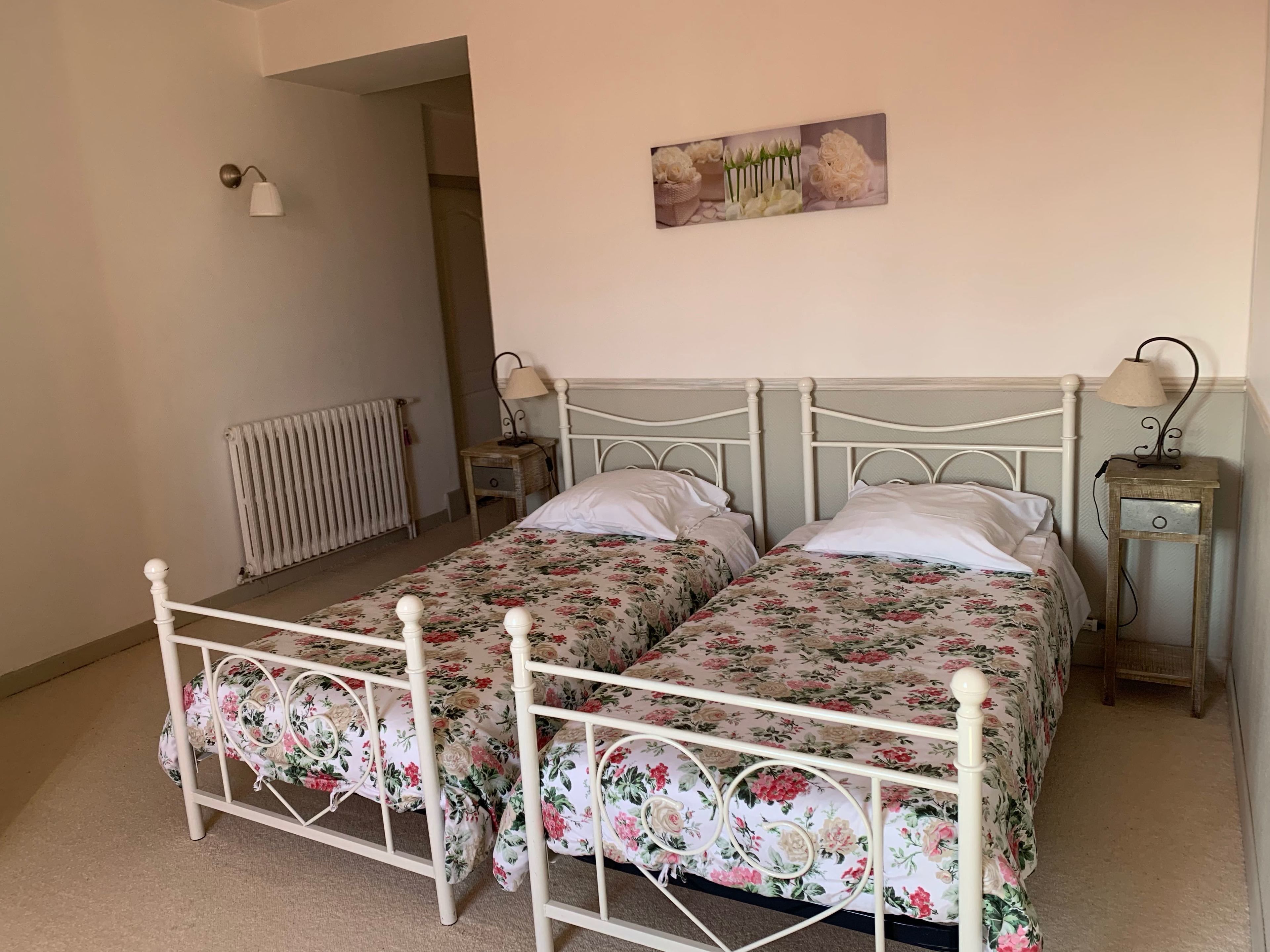Een tweepersoonsbed met bloemenbeddengoed, een nachtkastje met een lamp, een radiator en een foto aan de muur.