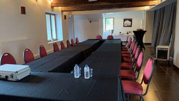 A conference room with a long table, red chairs, and a black tablecloth. There are water bottles on the table and a white suitcase on the floor.