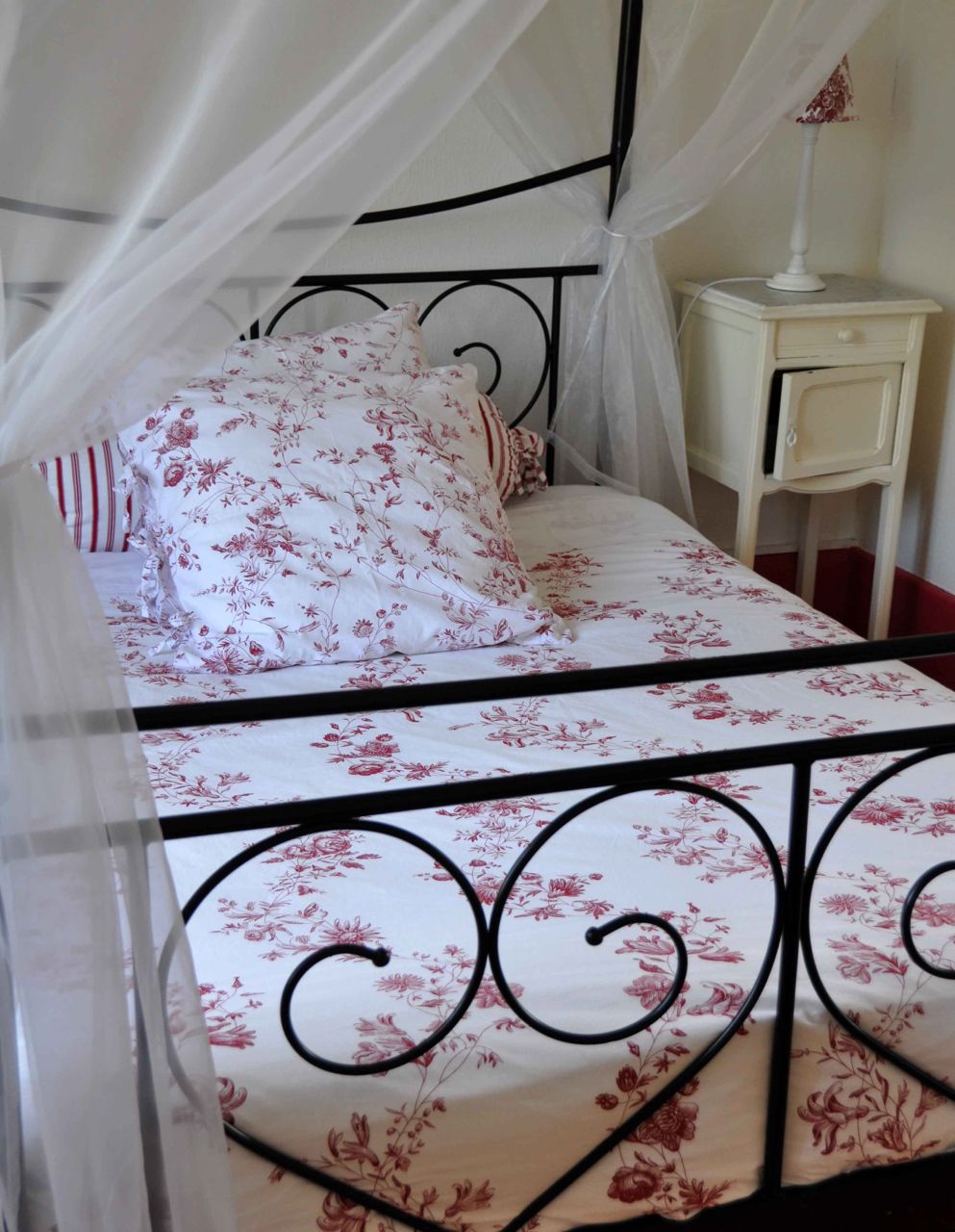 Een bed met een bloemenprint sprei, een witte nachtkastje en een hemelbed.