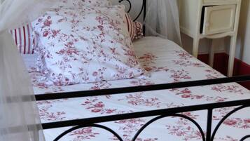 Een bed met een bloemenprint sprei, een witte nachtkastje en een hemelbed.