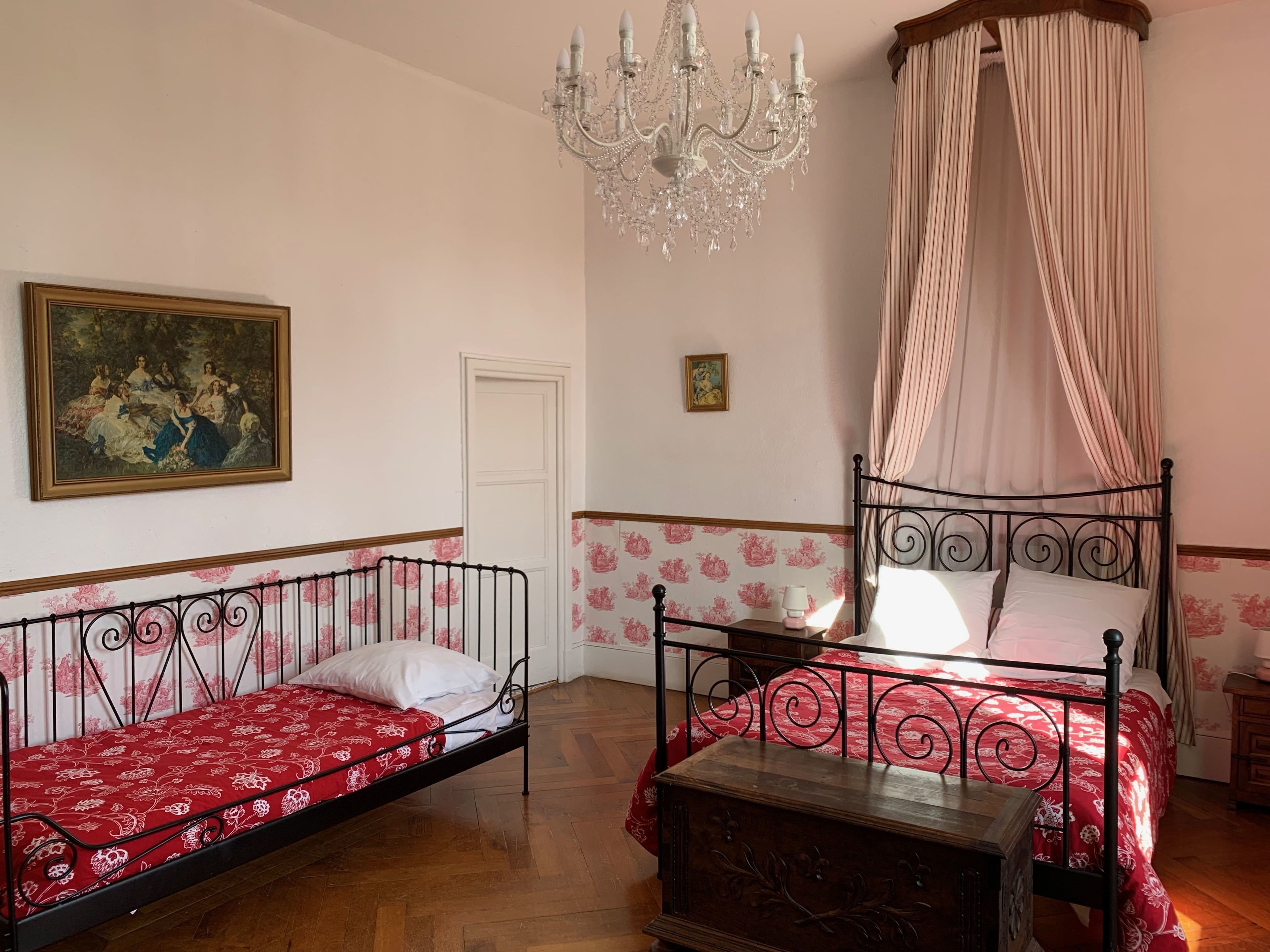 Une chambre à coucher avec un lit à baldaquin, une banquette, un lustre et un tableau au mur.