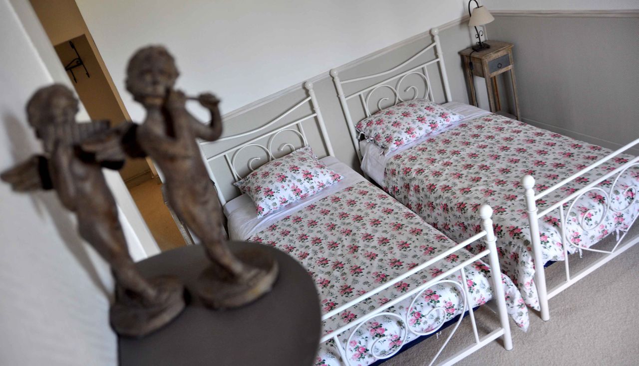 Ein Schlafzimmer mit zwei Betten, floralem Bettzeug, einem Nachttisch mit Lampe und einer Cherubstatue.