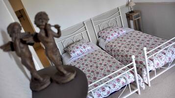 Un dormitorio con dos camas, ropa de cama floral, una mesita de noche con lámpara y una estatua de querubines.