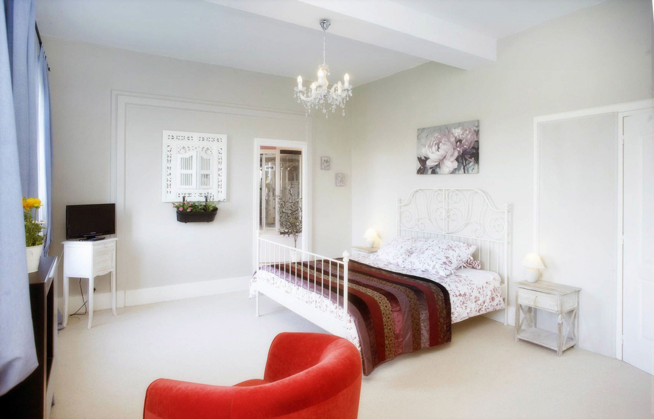 A bedroom with a bed, a red chair, a television, and a chandelier.