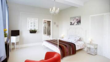A bedroom with a bed, a red chair, a television, and a chandelier.