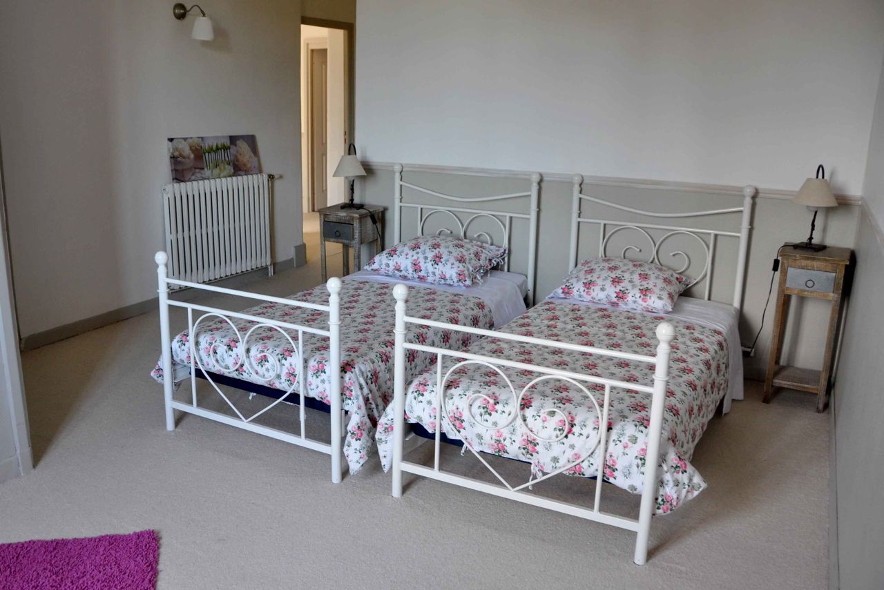 Une chambre avec deux lits simples, un radiateur, une petite table et une lampe.