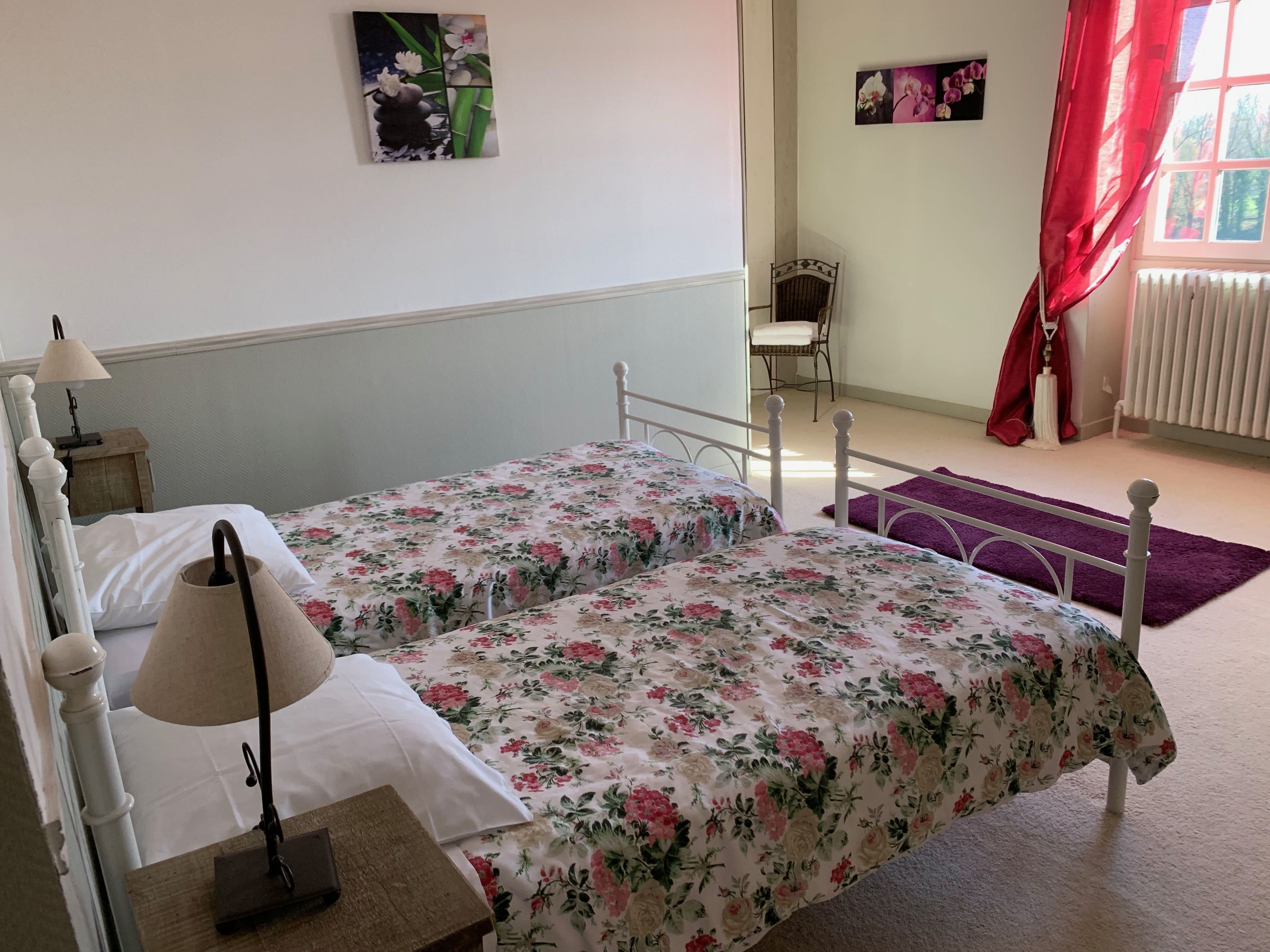 Un dormitorio con una cama doble, una mesita de noche, una lámpara, una silla y una ventana con cortinas rojas.