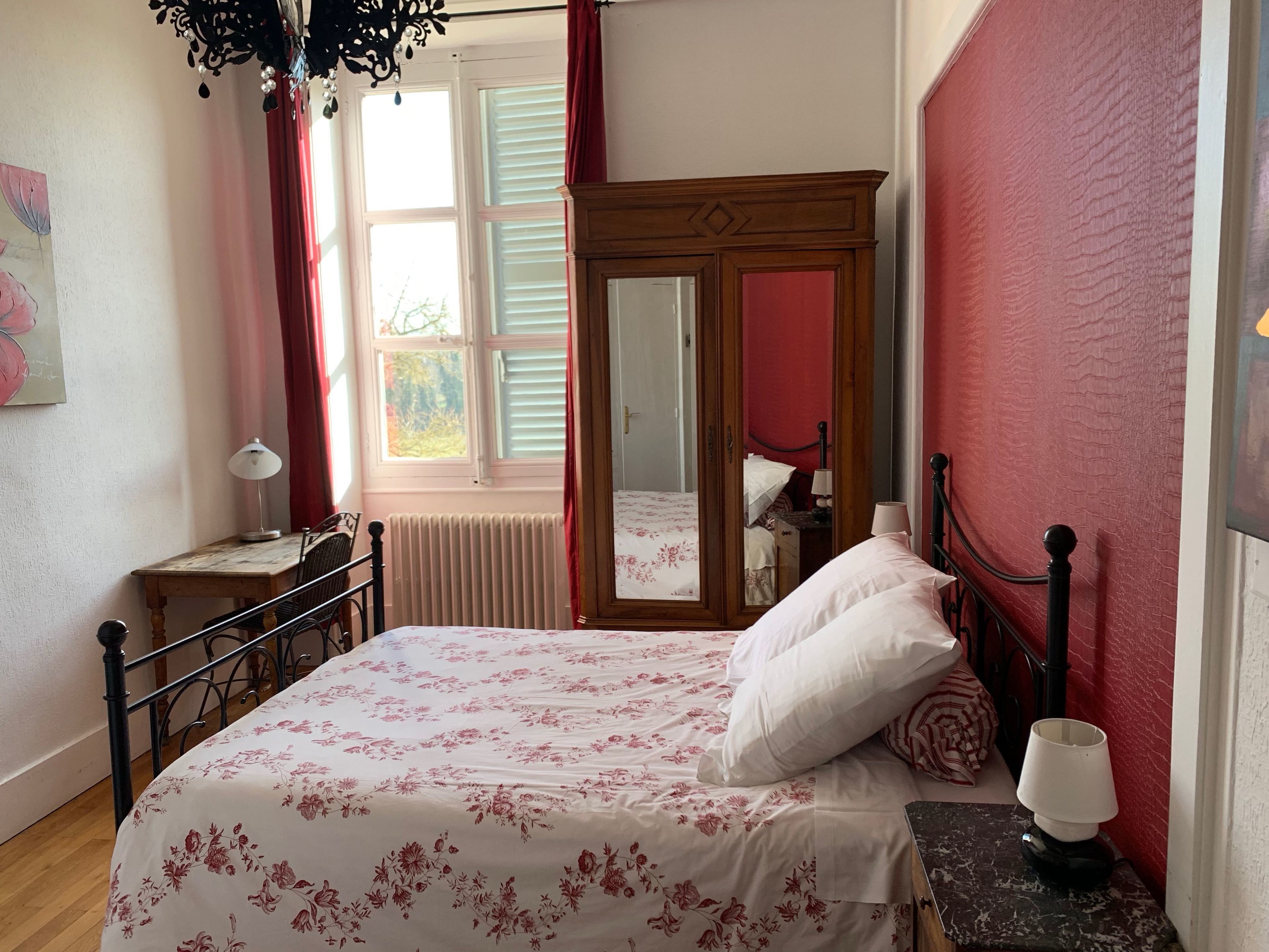 A bedroom with a bed, a nightstand, a dresser, a mirror, and a window with curtains.