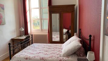 A bedroom with a bed, a nightstand, a dresser, a mirror, and a window with curtains.