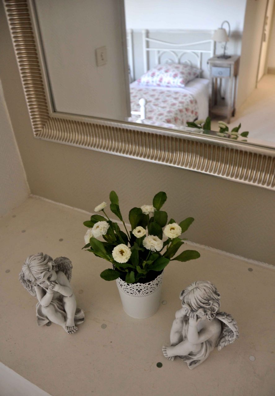 A bathroom vanity with a mirror, a white vase with flowers, and two angel figurines.