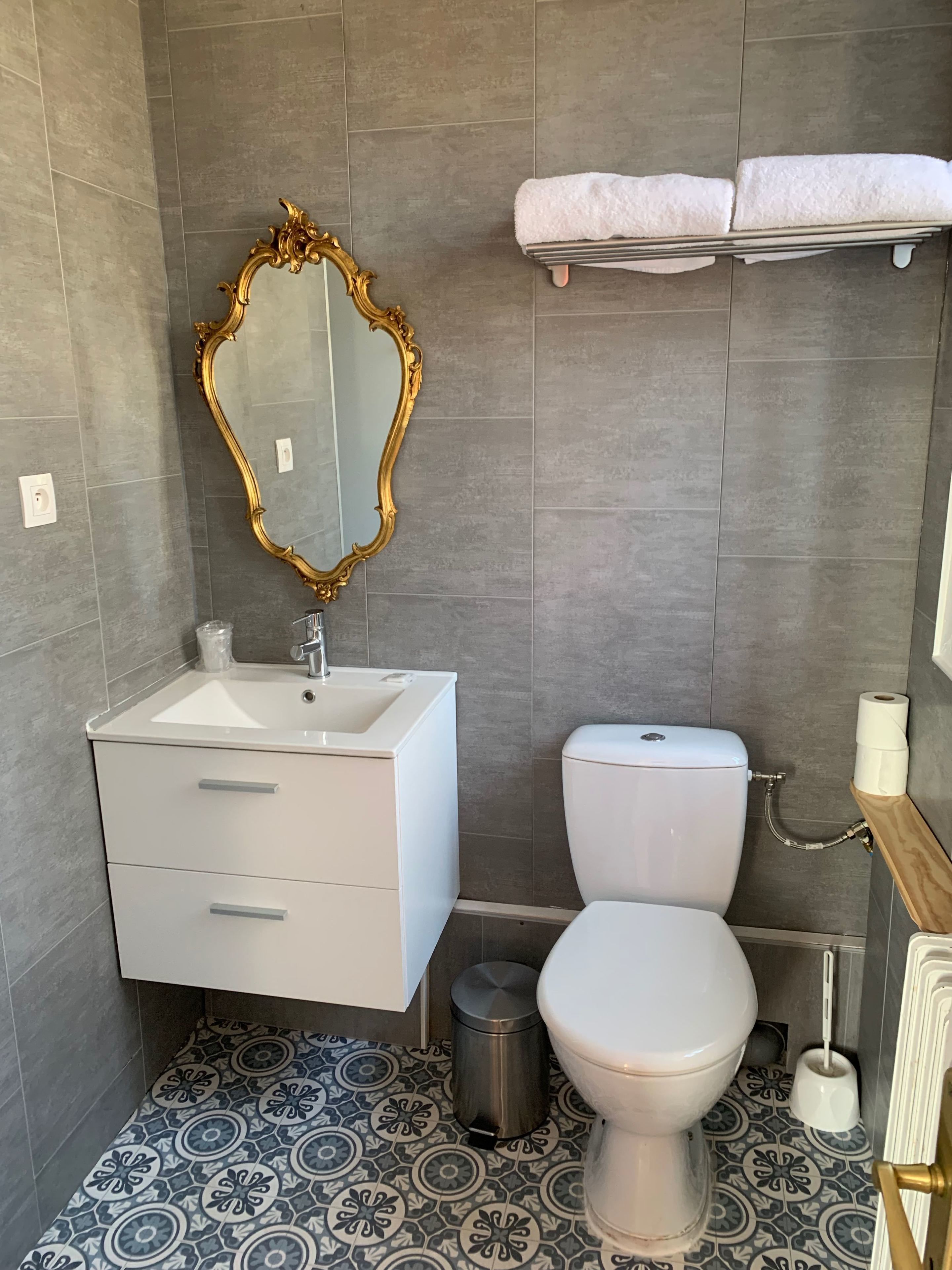 Un baño con un lavamanos blanco, un inodoro, un espejo con marco dorado y un perchero con dos toallas.