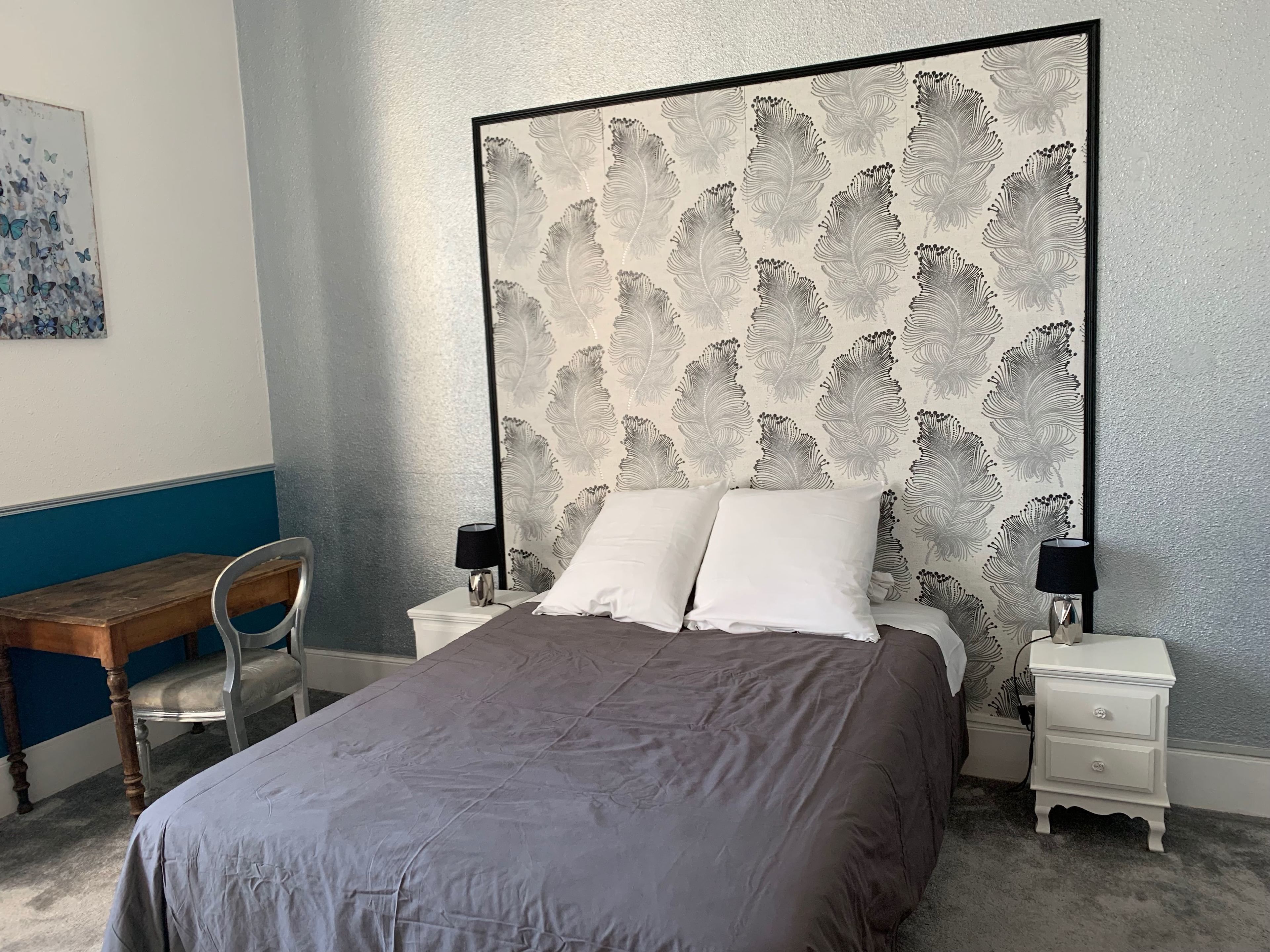 A bedroom with a large bed, two bedside tables, a chair, and a wall with a leaf pattern.