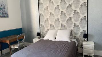 A bedroom with a large bed, two bedside tables, a chair, and a wall with a leaf pattern.