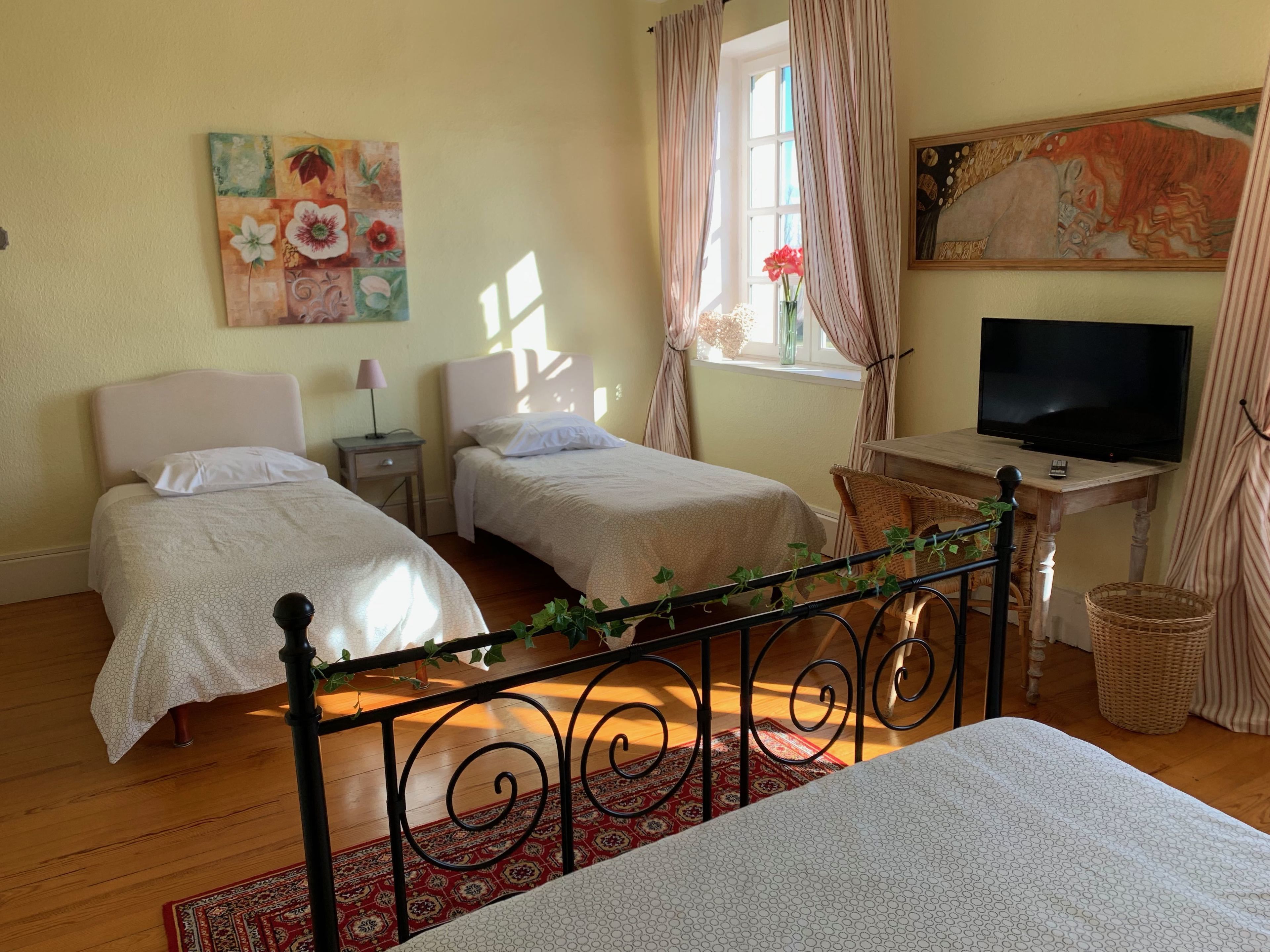 A bedroom with two beds, a TV, a painting, and a window with curtains.