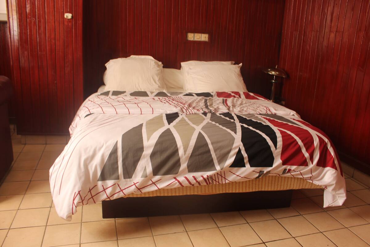 Una cama con colcha estampada, una lámpara de noche y un cabecero de madera.