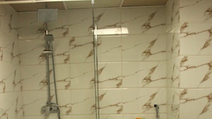 Et badeværelse med en glasafskærmet brusekabine, toilet og en væg med marmorlook.