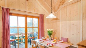 A wooden-paneled room with a dining table set for breakfast, featuring a view through large windows. - Lamplhof (Rimsting)
