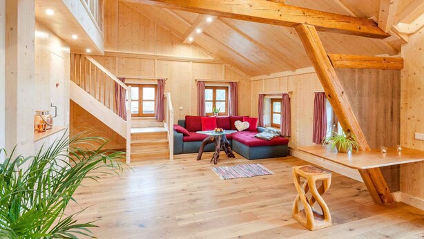 A spacious loft with a wooden interior, a red sofa, a dining table, and a staircase. - Lamplhof (Rimsting)