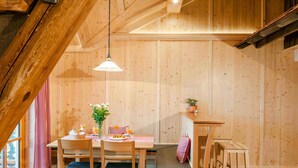 A wooden dining area with a table set for two, a hanging light fixture, and a window with a checkered curtain. - Lamplhof (Rimsting)
