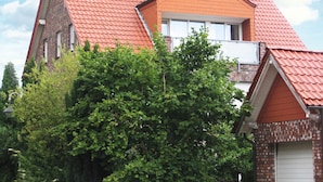 A two-story house with a red-tiled roof, a visible chimney, and a small window on the upper floor.