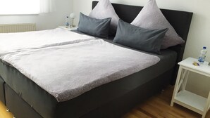 A double bed with grey bedding, a black headboard, and two bedside tables with water bottles.