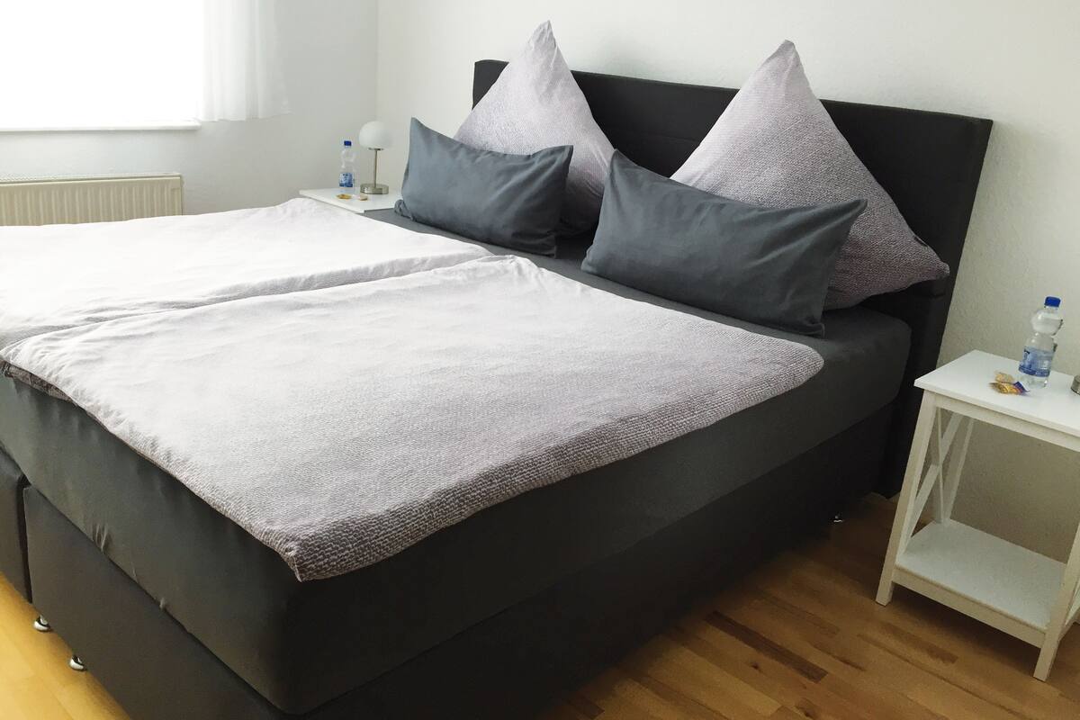 A double bed with grey bedding, a black headboard, and two bedside tables with water bottles.