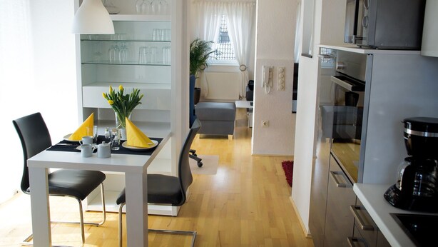 A modern kitchen with a microwave, oven, and coffee maker. There is a dining area with a table, chairs, and a vase of flowers.