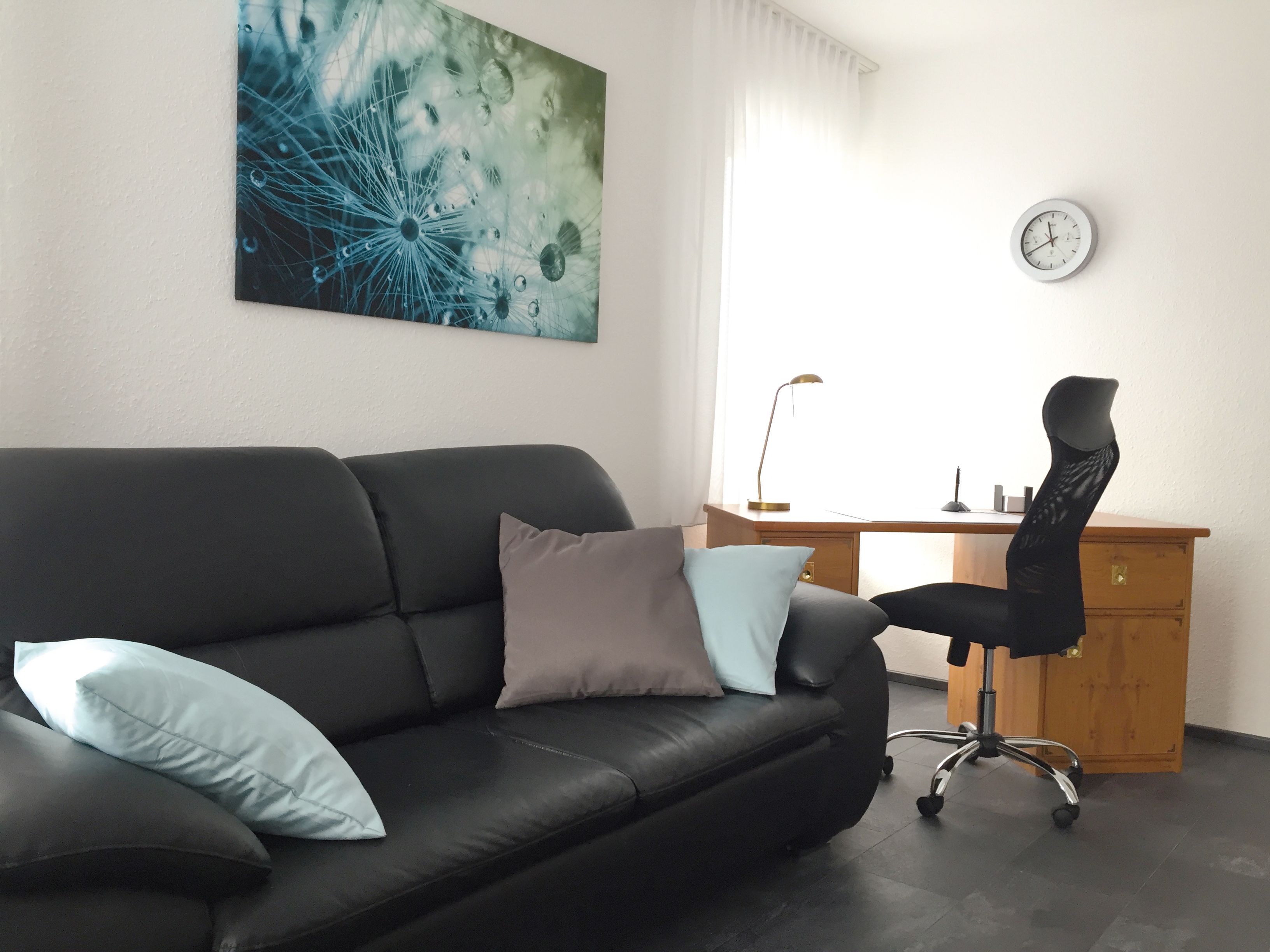 Ein modernes Wohnzimmer mit einem schwarzen Ledersofa, einem Holztisch und einem schwarzen Bürostuhl.