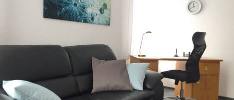 Ein modernes Wohnzimmer mit einem schwarzen Ledersofa, einem Holztisch und einem schwarzen Bürostuhl.
