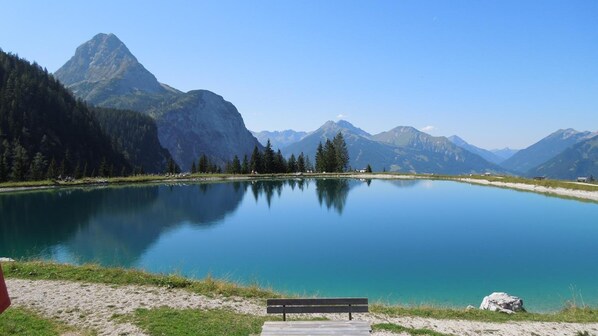 Ein friedlicher See mit einer Bank im Vordergrund, umgeben von Bergen und Bäumen.