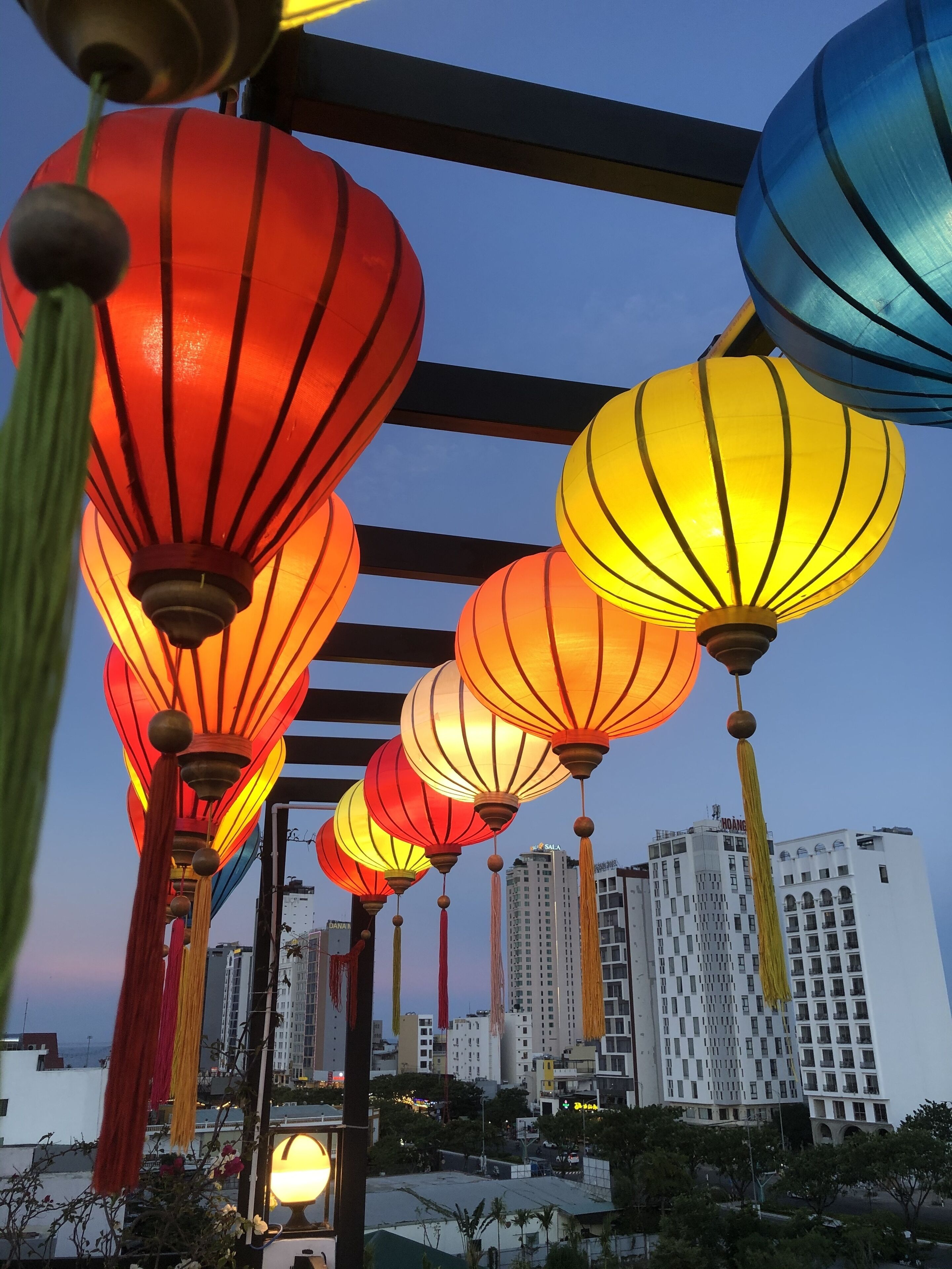 A row of colorful lanterns hanging outdoors with a cityscape in the background.