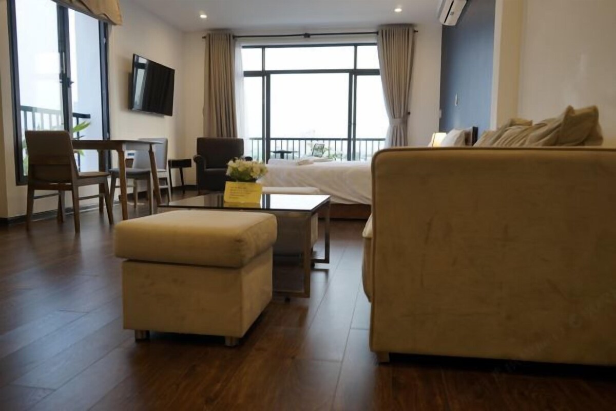 A modern hotel room with a sofa, ottoman, TV, and a balcony view.