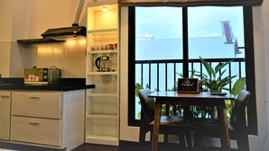 A kitchen with white cabinets, a black countertop, and a window with a view of the sea. There is a table with chairs and a sign that says "WiFi Password." - Oasis Hotel & Apartment (Da Nang)