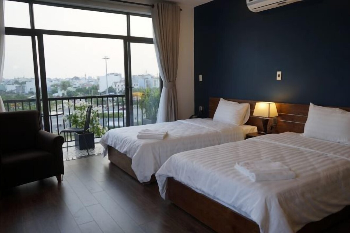 A hotel room with two beds, a view of the city, and a balcony with a chair.