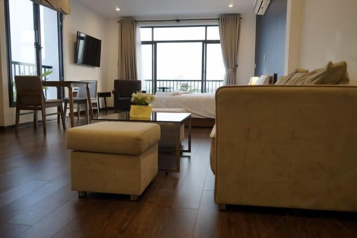 A modern hotel room with a sofa, ottoman, TV, and a balcony view.